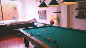 Uma mesa de bilhar com bolas, uma luminária e obras de arte nas paredes.