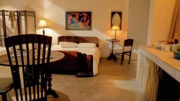 Habitación de hotel con cama, escritorio, silla, lámpara y un cuadro en la pared.