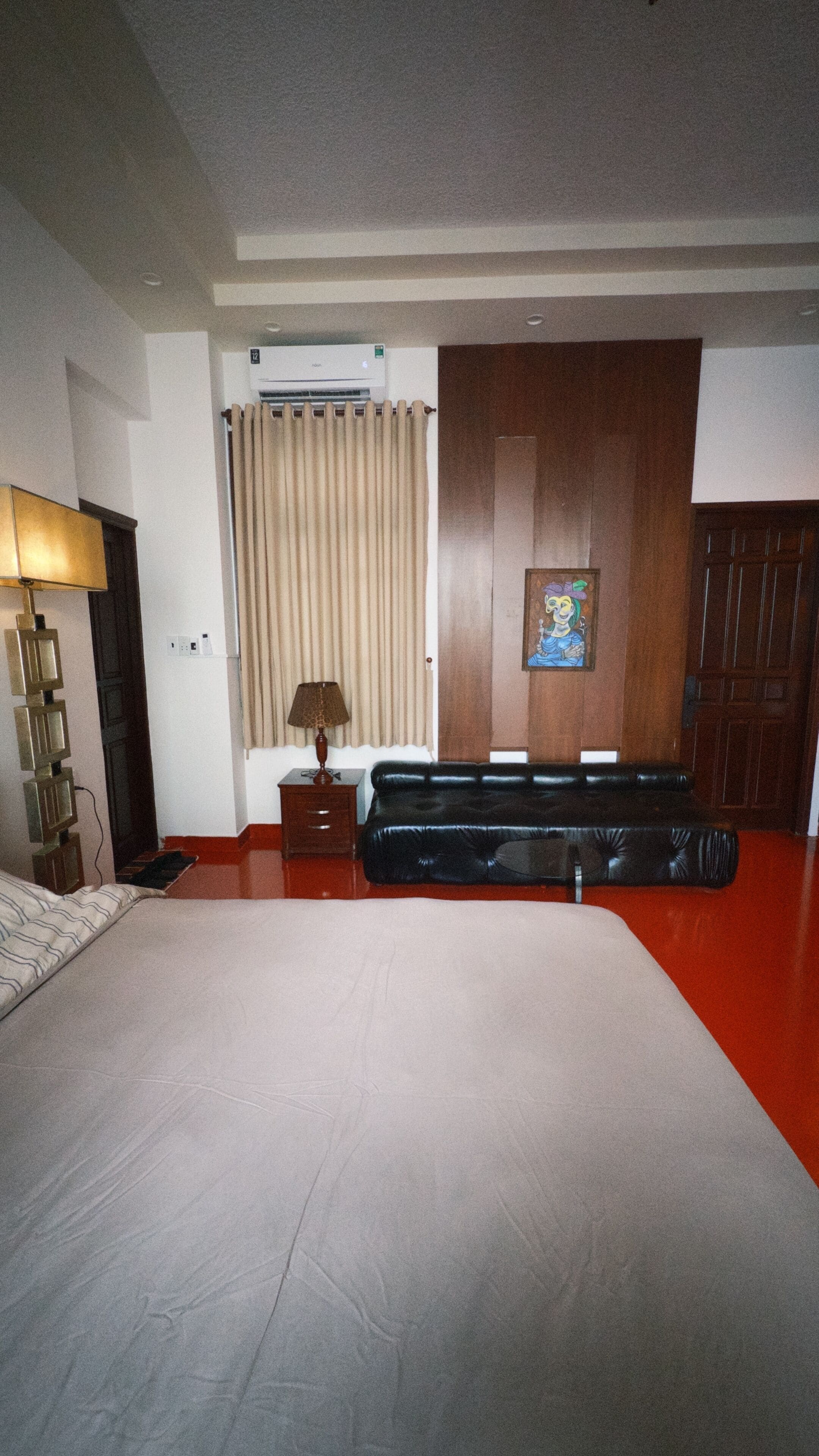 Una habitación de hotel con cama, un armario de madera, una lámpara, un cuadro y una ventana con cortinas.