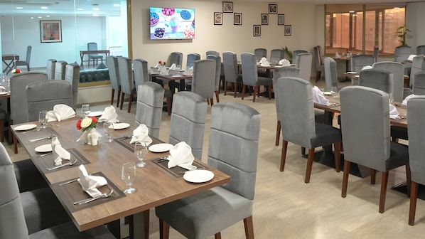 A dining area with multiple tables set for service, grey upholstered chairs, and a television mounted on the wall.