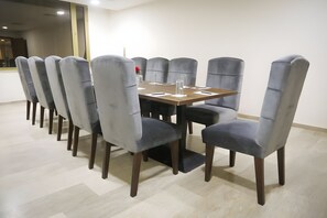 Una sala de conferencias con una mesa rectangular, sillas tapizadas en gris y suelo de madera.