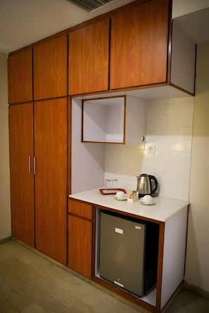 A compact kitchen with wooden cabinets, a white countertop, a small refrigerator, and a kettle.