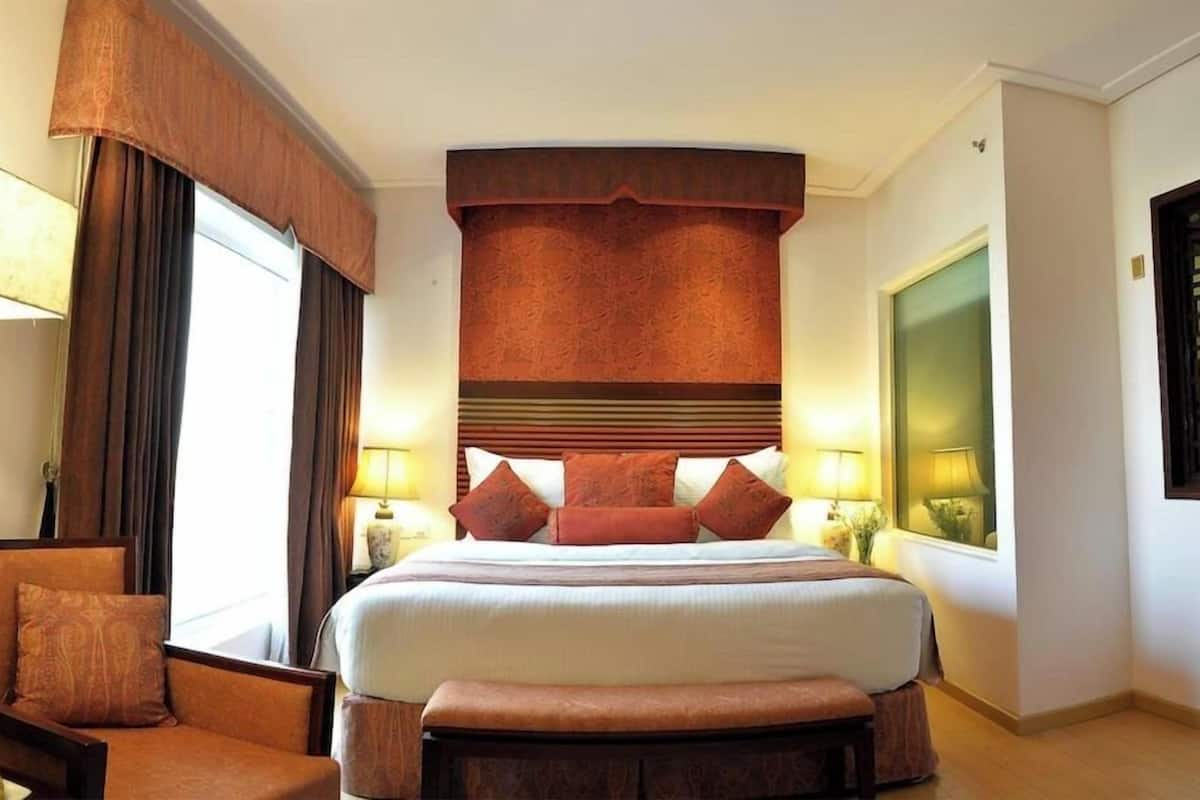 A hotel room with a large bed, a chair, a bench, and a window with curtains.