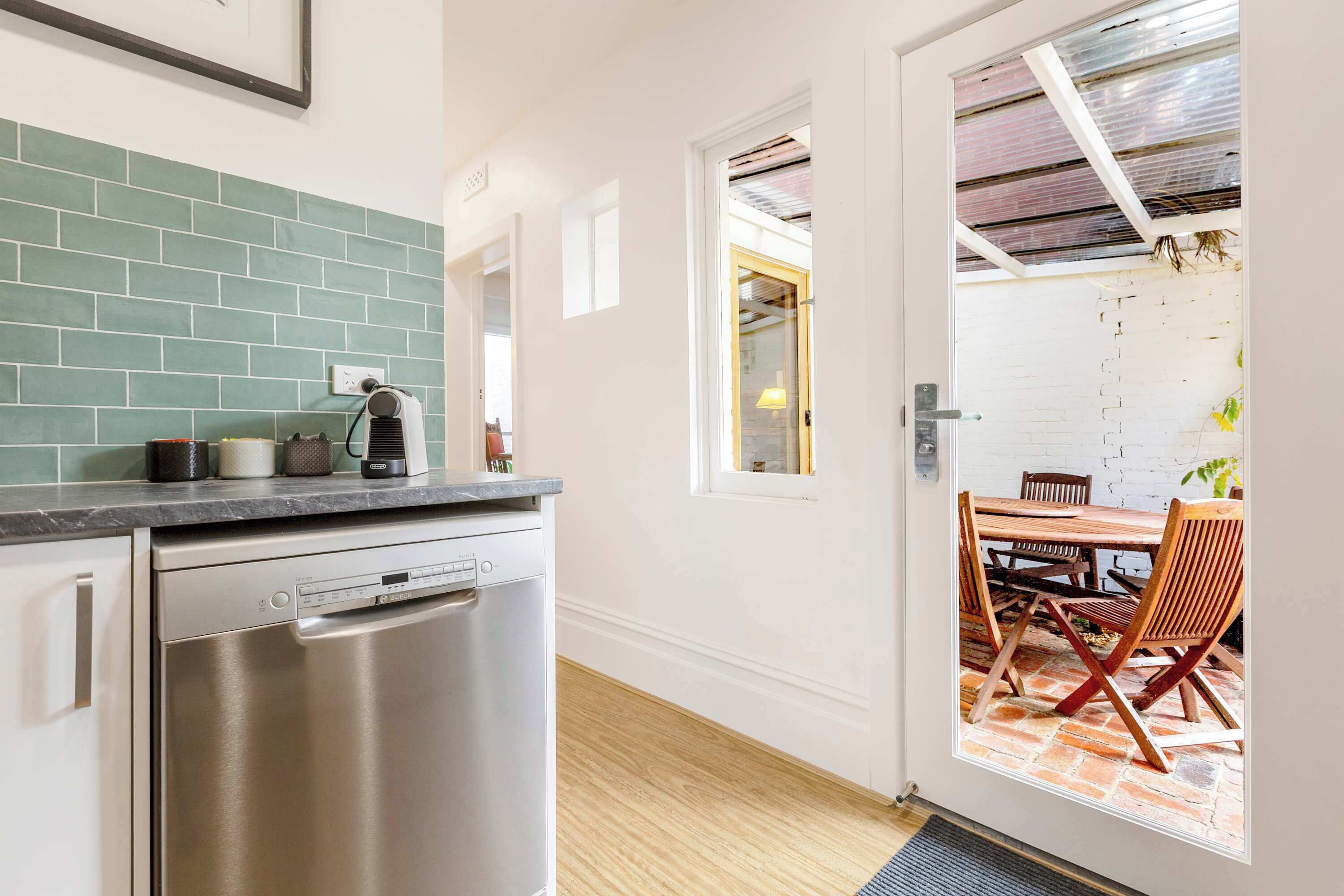 A kitchen with a dishwasher, a countertop with kitchen items, and a dining area with a table and chairs.
