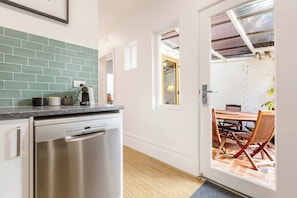 A kitchen with a dishwasher, a countertop with kitchen items, and a dining area with a table and chairs. - Storied terrace opposite Carlton Gardens (Carlton)