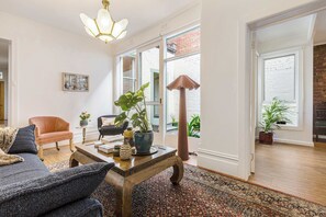 A living room with a sofa, armchair, coffee table, and potted plants. - Storied terrace opposite Carlton Gardens (Carlton)