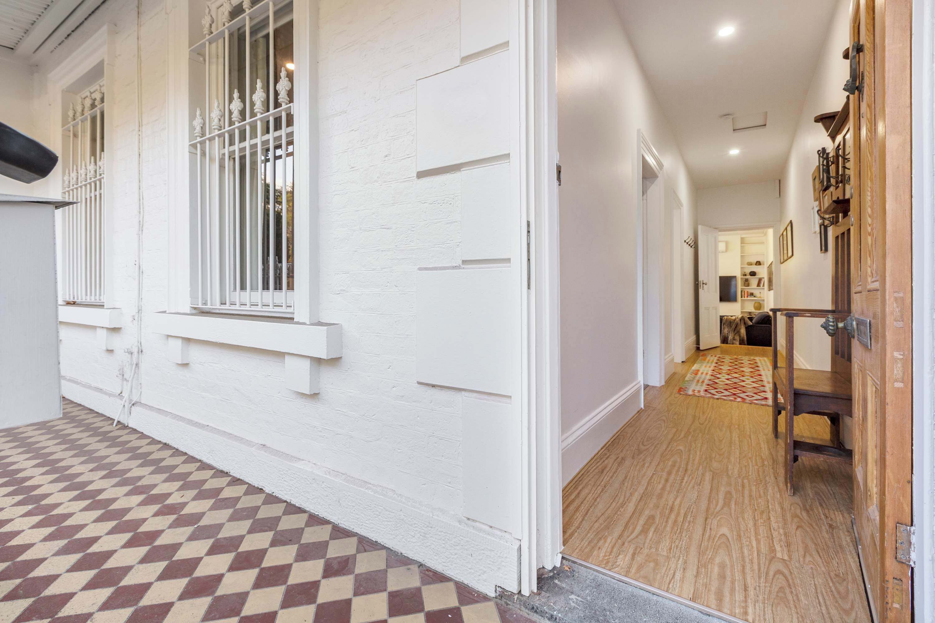 A hallway with a checkered floor, white walls, and a wooden door.
