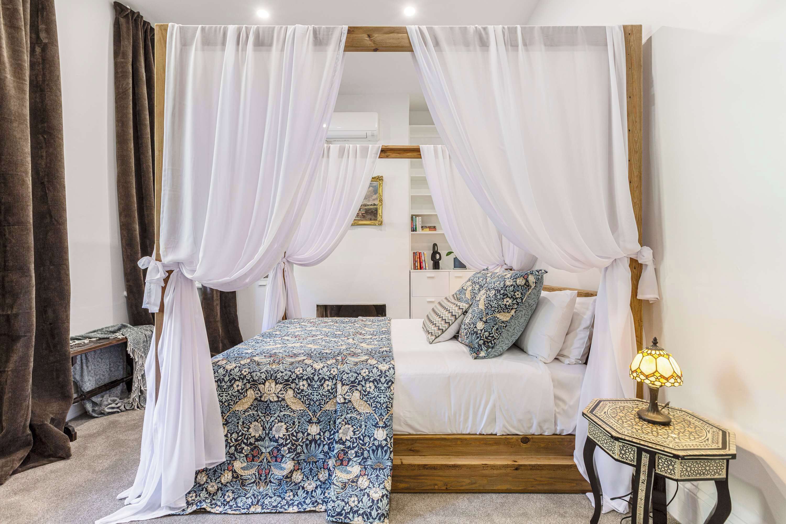 A bedroom with a canopy bed, a bedside table with a lamp, and a small wooden nightstand.