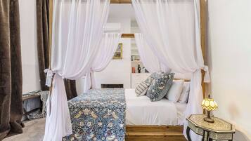 A bedroom with a canopy bed, a bedside table with a lamp, and a small wooden nightstand.
