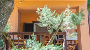 Un balcone con ringhiera in legno, un albero in vaso e un edificio con pareti arancioni e una finestra.