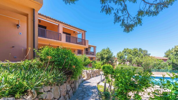 Un edificio a più piani con balconi, un vialetto in pietra e una piscina.