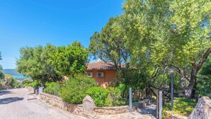Un sentiero a muri di pietra conduce a una casa con tetto in tegole, immersa nel verde e tra alberi.