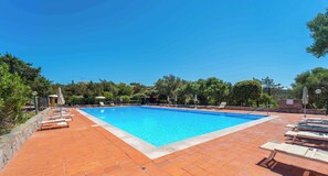 Ein rechteckiger Swimmingpool mit klarem, blauem Wasser, umgeben von einer gefliesten Liegefläche mit Liegestühlen und Sonnenschirmen.