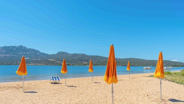 Une plage avec plusieurs parasols orange et une seule chaise de plage rayée de bleu et de blanc.