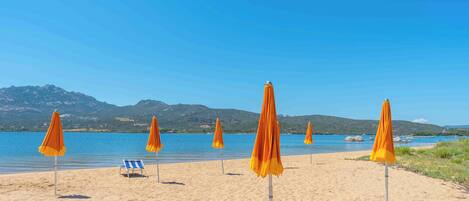 A beach with several orange umbrellas and a single blue and white striped beach chair.