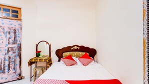 A bedroom with a bed, a wooden headboard, a bedside table with a mirror, and a chair. - Spot On 91512 Siantan Anambas Syariah (Batam)