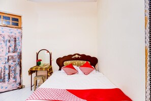 A bedroom with a bed, a wooden headboard, a bedside table with a mirror, and a chair. - Spot On 91512 Siantan Anambas Syariah (Batam)