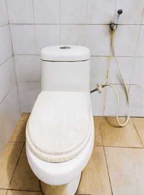 Inodoro con asiento y tapa blancos, una palanca de descarga visible y una manguera unida a la pared.