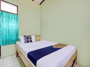 Un lit simple avec une couvre-lit blanche et bleue, deux oreillers à motifs géométriques, un rideau de couleur turquoise et une tête de lit en bois.