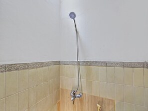 Une douche équipée d’un pommeau de douche à main, d’un robinet mural et d’un sol carrelé.