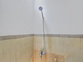 Um chuveiro com um chuveiro manual, uma torneira fixada na parede e um chão revestido de azulejos.
