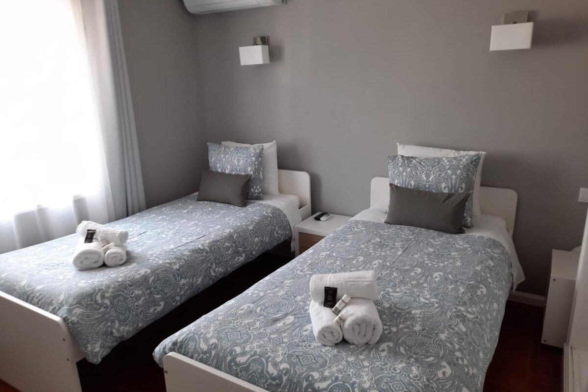 Two twin beds with patterned bedding, bedside tables, and a wall-mounted air conditioner.