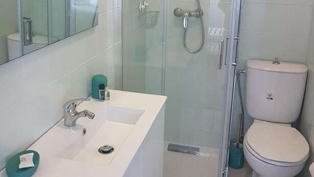 A modern bathroom with a glass-enclosed shower, a white sink with a mirror above, and a toilet. - See U Inn (Murtosa)