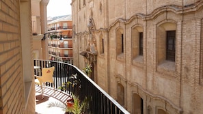 A balcony with a view of adjacent buildings, including a brick structure with arched windows and a yellow chair. - Hotel Mesv N El Nv Mero Uno (Antequera)