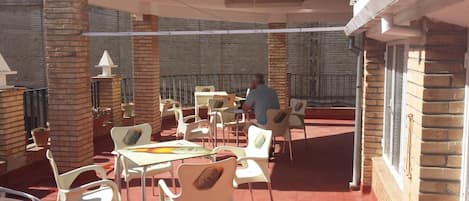 An outdoor patio with tables and chairs, a person seated at a table, and a brick building in the background.