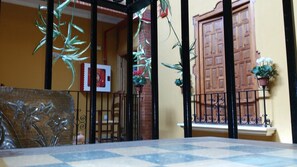 A room with a checkered floor, a metal railing, a wooden door, and hanging plants. - Hotel Mesv N El Nv Mero Uno (Antequera)