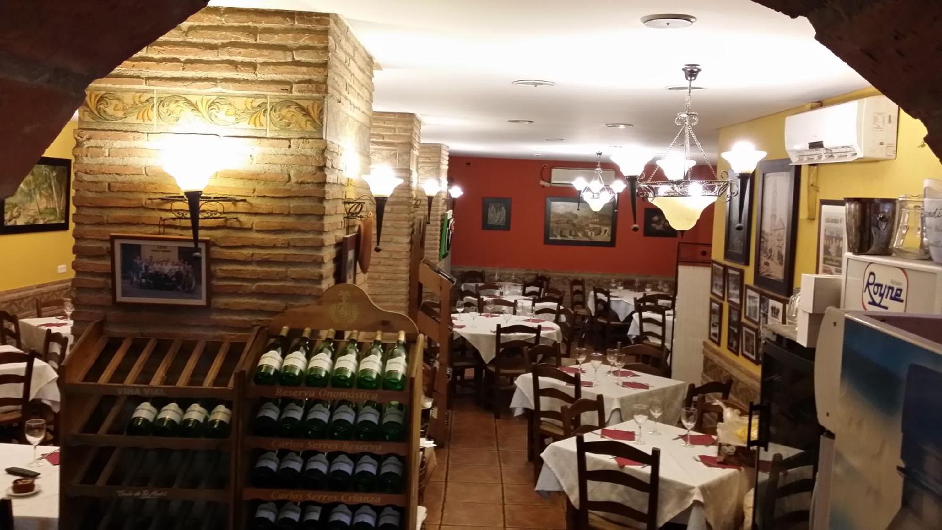 Interior de restaurante com paredes de pedra, várias mesas e garrafas de vinho expostas.