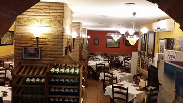 Interior de restaurante con paredes de piedra, varias mesas y botellas de vino exhibidas.
