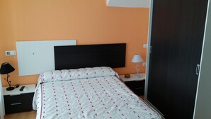 Hotellihuone, jossa on sänky, yöpöytä, lamppu, vaatekaappi ja seinälle asennettu televisio.