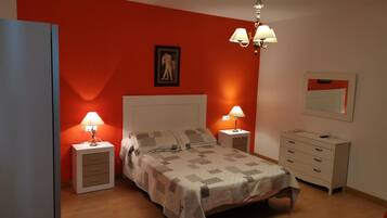 Un dormitorio con una cama, dos mesitas de noche con lámparas, un aparador, un espejo y una pared de acento roja.