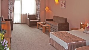 Une chambre d’hôtel avec un lit, deux fauteuils, un canapé, une petite table, une lampe et un tableau au mur.