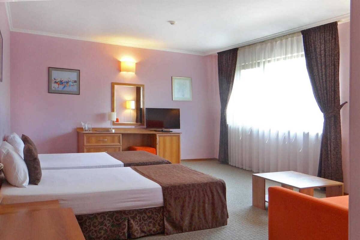 A hotel room with two beds, a desk, a television, and a small table.