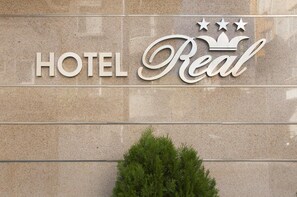 Ein Schild für 'HOTEL Real' mit schlichtem, klaren Design und drei Sternen über dem Wort 'Real'.