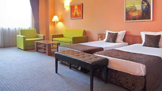 Une chambre d’hôtel avec deux lits, un canapé, une table basse et un banc.