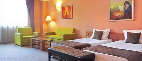 Habitación de hotel con dos camas, un sofá, una mesa de centro y un banco.
