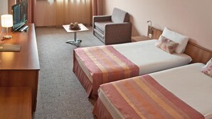 Une chambre d’hôtel avec deux lits, un bureau, une chaise, une petite table et un téléviseur.