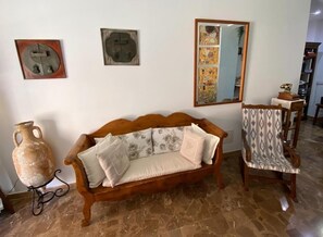 Een kamer met een houten bank, een gestreept fauteuil, een grote vaas en twee kunstwerken aan de muur.