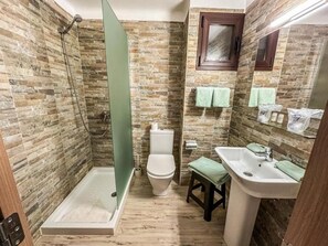 Baño con ducha, inodoro y lavamanos, con paredes con diseño de piedra y un armario de madera.