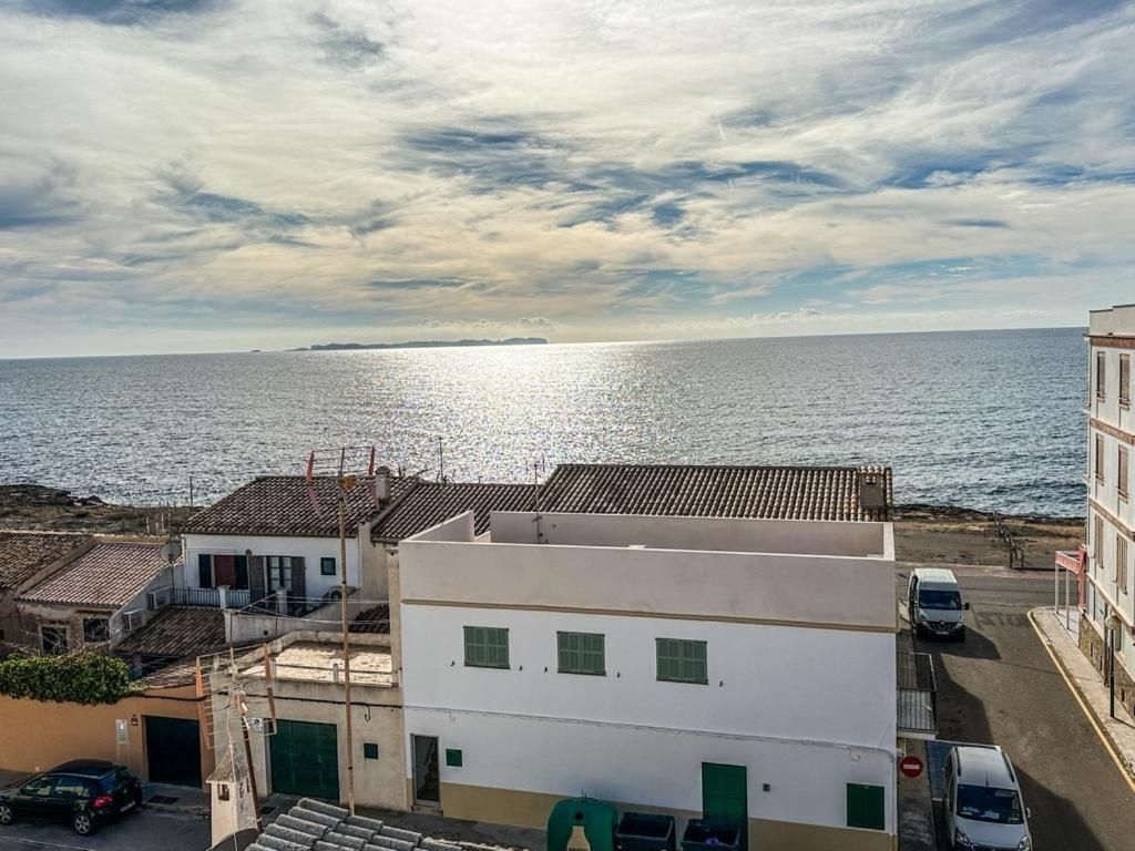 Un edificio costero con vista al mar, una calle con coches aparcados y un cielo despejado.