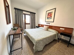 A hotel room with a bed, a bedside table, a chair, a small table with a plant, a framed picture on the wall, and a window with curtains. - Hostal Ca N Pep (Campos)