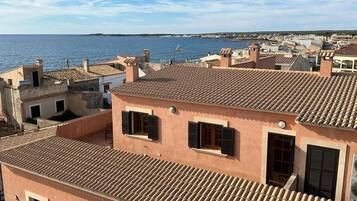 A coastal residential area with terracotta-tiled rooftops and a view of the sea.