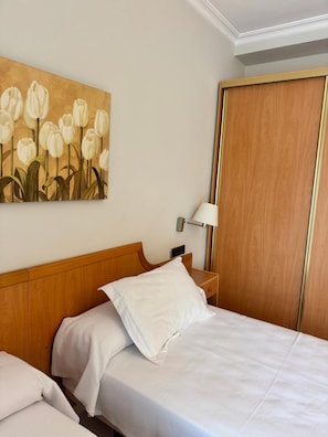 A hotel room with a bed, a nightstand, a lamp, and a painting of white tulips on the wall. - El Eden (El Ejido)