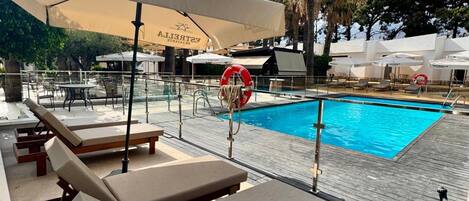A poolside area with lounge chairs, umbrellas, and a lifebuoy.