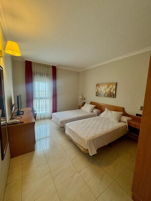 A hotel room with two beds, a desk with a computer, and a window with curtains. - El Eden (El Ejido)