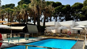 A swimming pool with a wooden deck, surrounded by palm trees and umbrellas. - El Eden (El Ejido)
