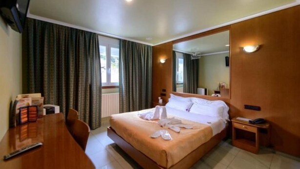 Een hotelkamer met een bed, een bureau, een stoel, een nachtkastje, een spiegel en een raam met gordijnen.